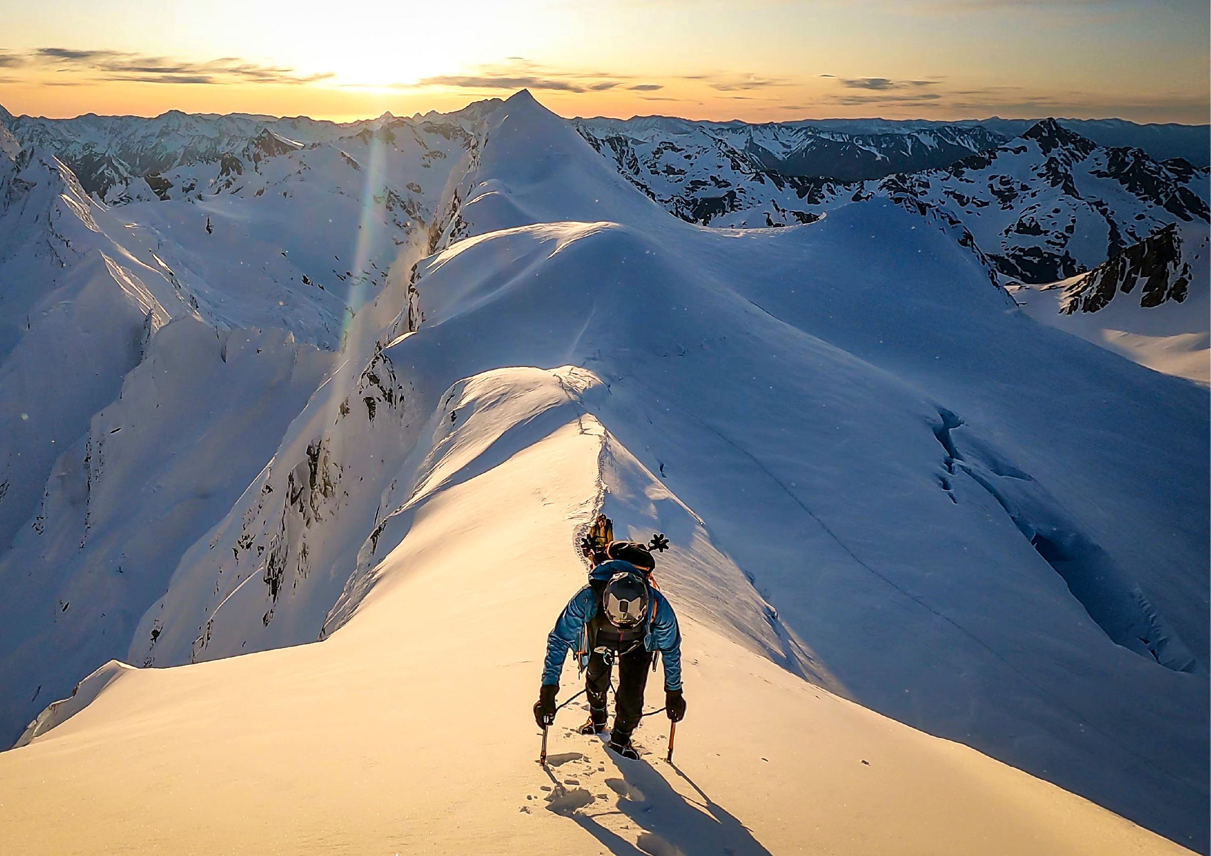 Climber ascending a snow ridge at golden sunset, peaks and glaciers stretching to the horizon