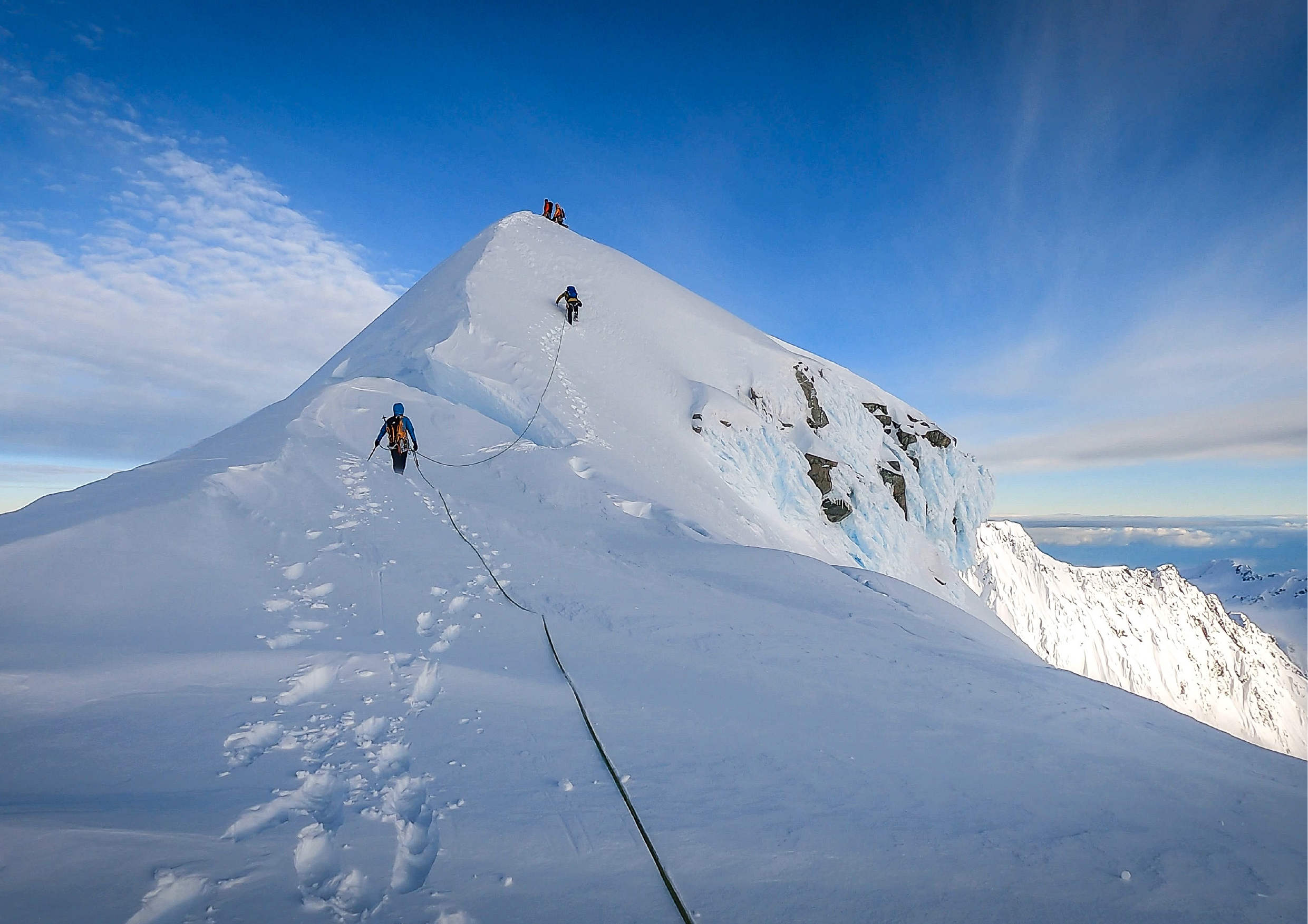 Rope team climbing the final ridge to a summit on a clear blue sky day